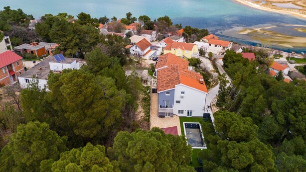 Μια αεροφωτογραφία μιας παραθαλάσσιας οικιστικής περιοχής, με σπίτια, μια παραλία και μια μεγάλη έκταση νερού.
