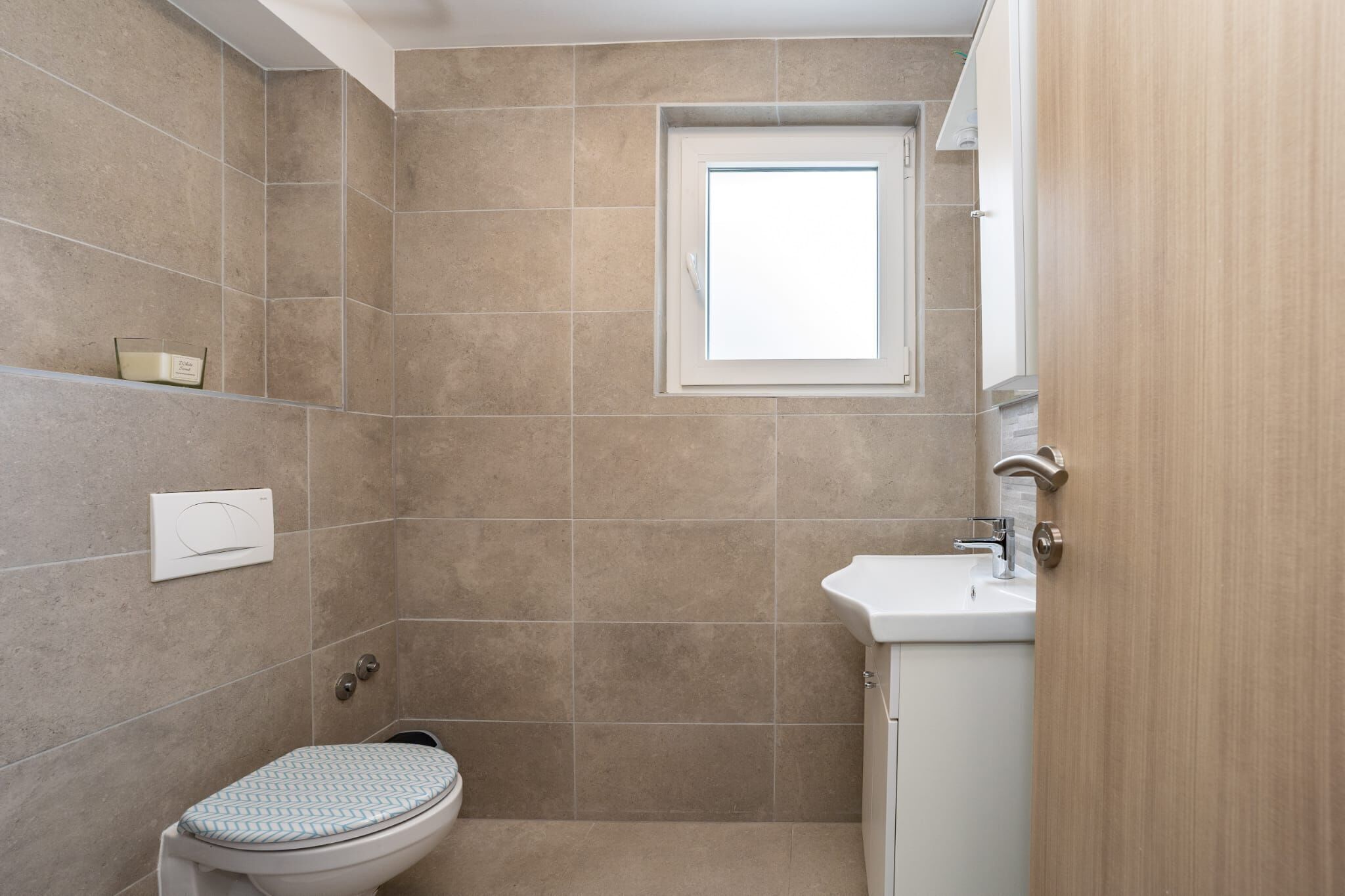 A small bathroom with a toilet, a sink, and a window.