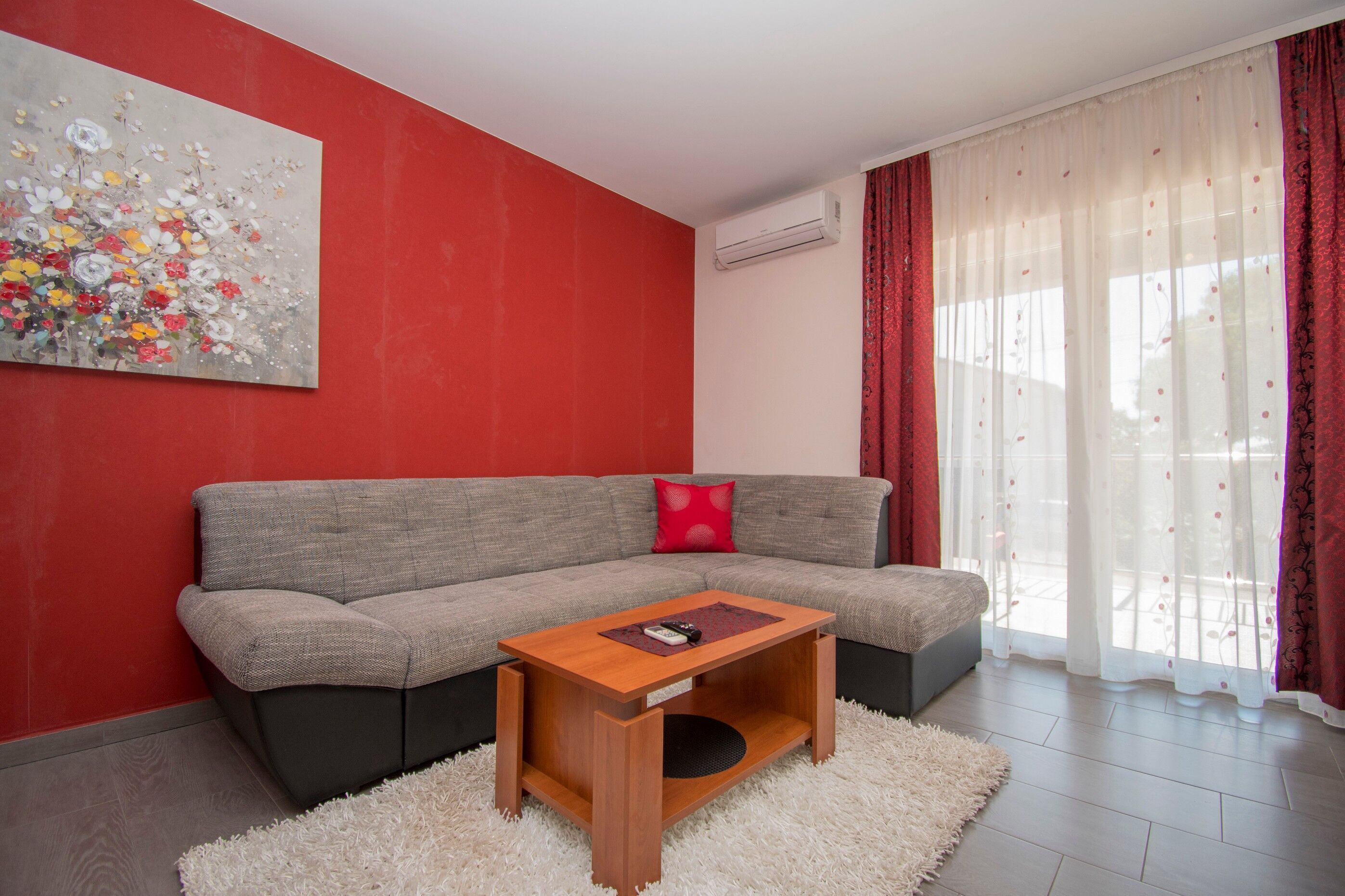 Un salon moderne avec un canapé gris, une table basse en bois et un mur rouge.