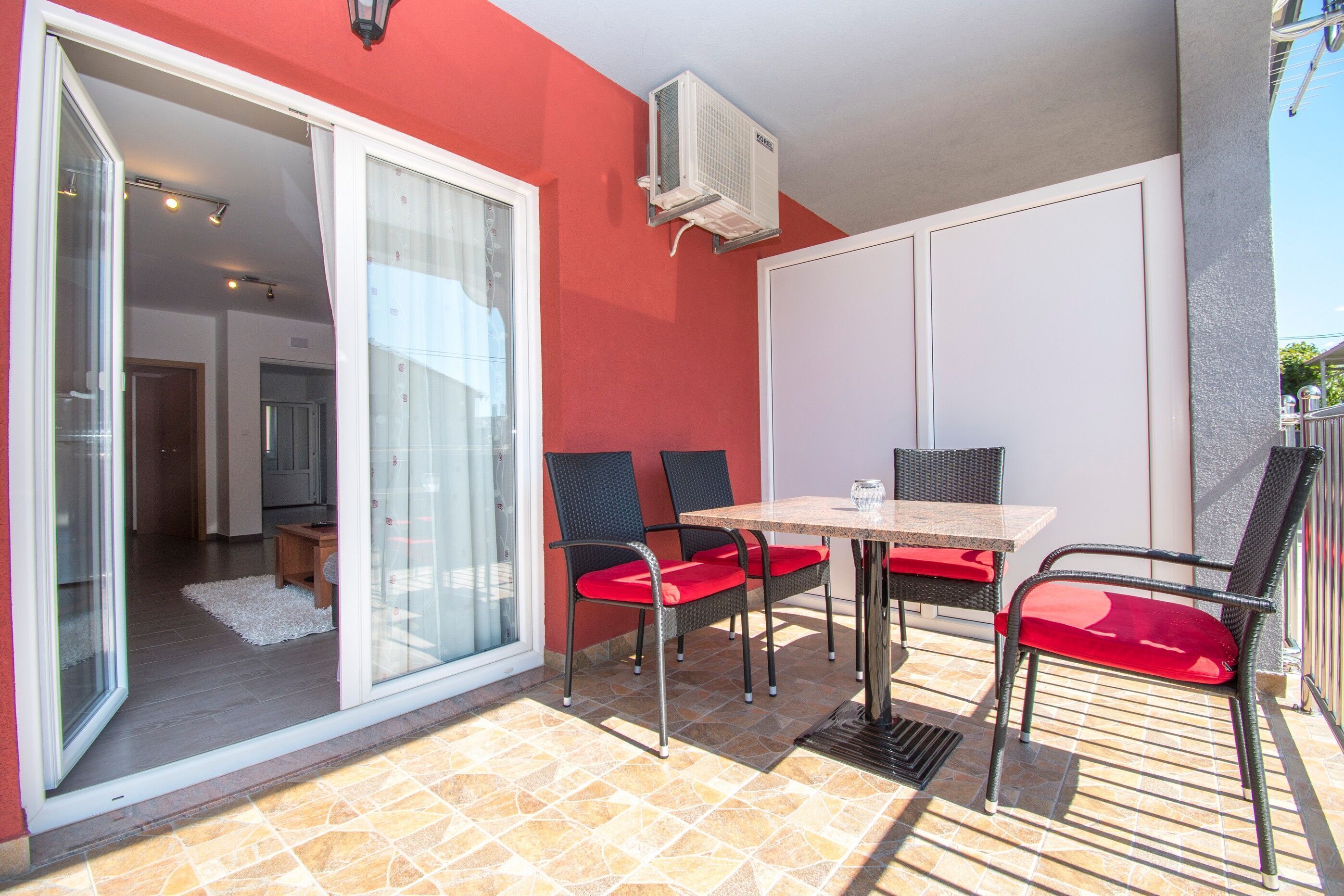 Een buitenterras met een tafel en stoelen, een schuifdeur die leidt naar een binnenruimte en een airconditioning op de muur.