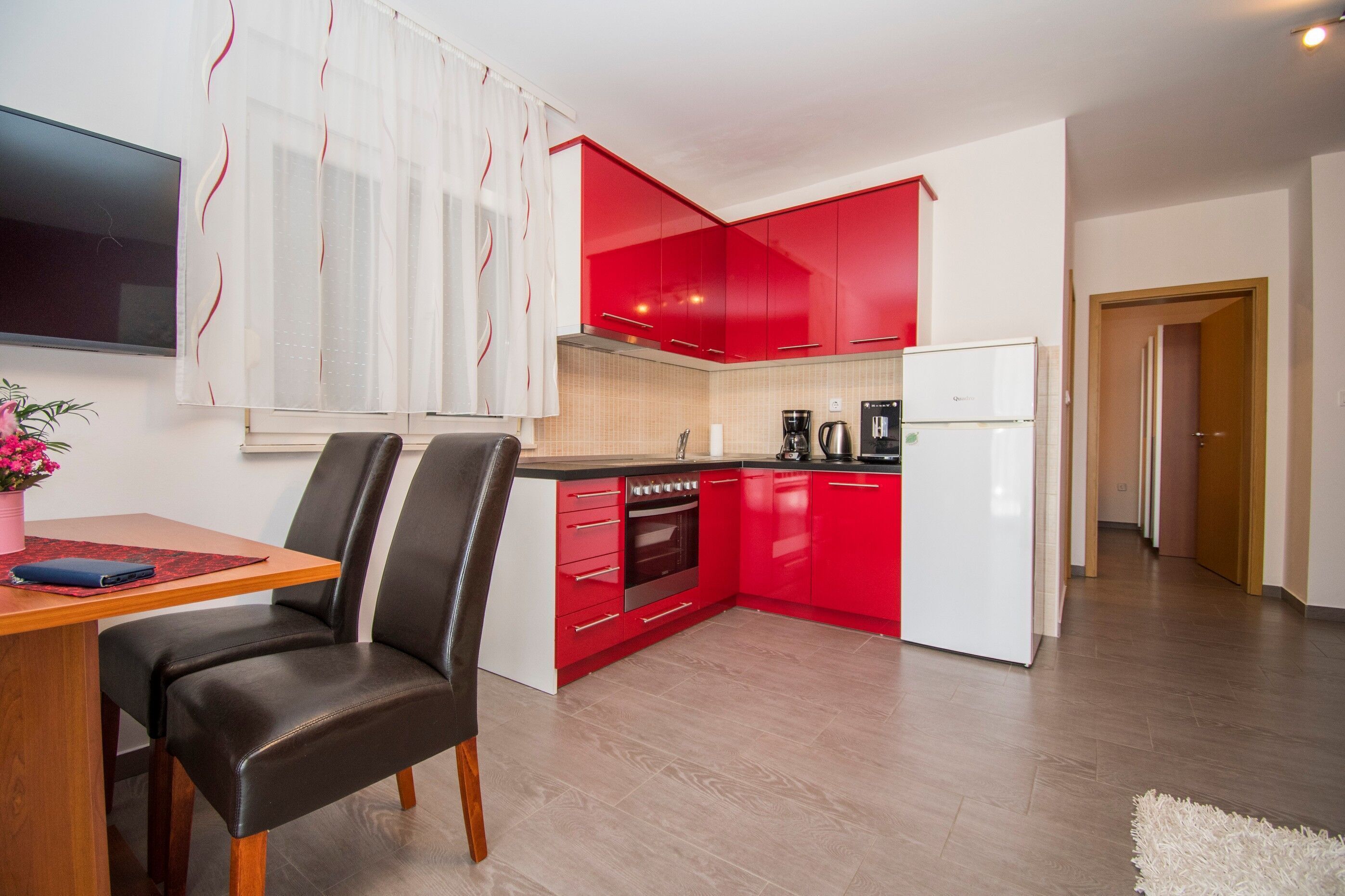 A modern kitchen with red cabinets, a white refrigerator, and a dining area with a table and chairs.