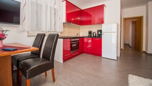 A modern kitchen with red cabinets, a white refrigerator, and a dining area with a table and chairs. - Apartments AS (Vodice)