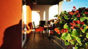 A covered outdoor area with a red wall, a table with chairs, and a potted plant with red flowers. - Apartments AS (Vodice)