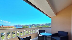 A balcony with wicker furniture, a small round table, and a view of a lake and mountains. - Apartments Dijana (Lopar)