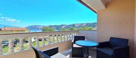 A balcony with wicker furniture, a small round table, and a view of a lake and mountains.