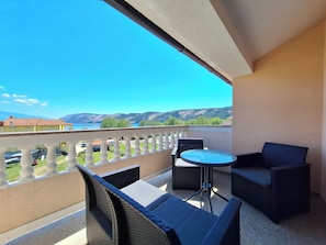 Un balcon agrémenté de meubles en osier, une petite table ronde et une vue sur un lac et des montagnes.