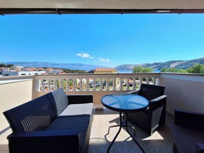A balcony with a table and two chairs, overlooking a scenic view of mountains and a body of water. - Apartments Dijana (Lopar)