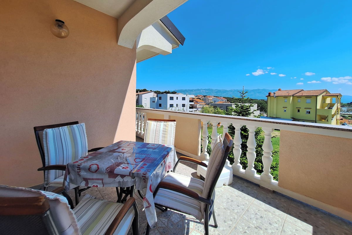 A balcony with a table and chairs, a view of buildings, and a clear sky.