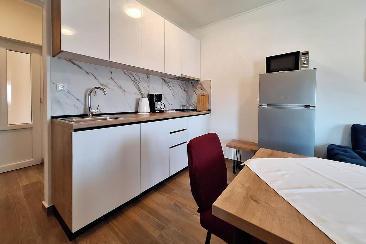 A modern kitchen with white cabinets, a marble backsplash, a sink, a coffee maker, and a refrigerator.
