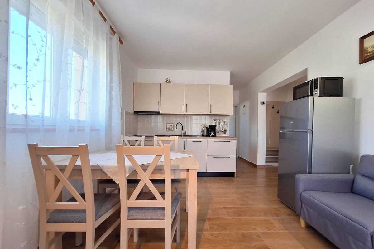 A modern kitchen with white cabinets, a dining table with chairs, a sofa, and a refrigerator.