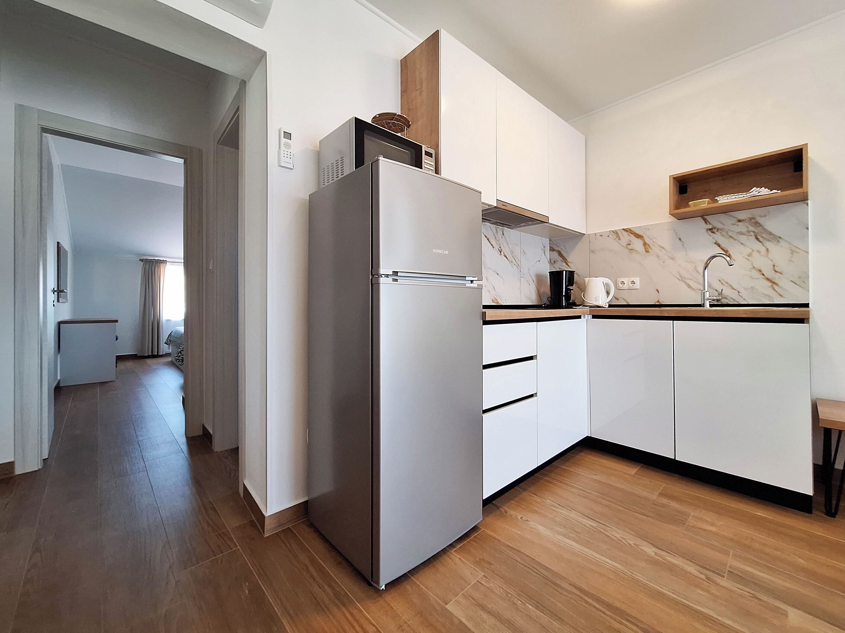 Una cocina moderna con armarios blancos, un refrigerador de acero inoxidable, una encimera de mármol y piso de madera.