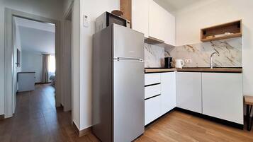 Una cocina moderna con armarios blancos, un refrigerador de acero inoxidable, una encimera de mármol y piso de madera.