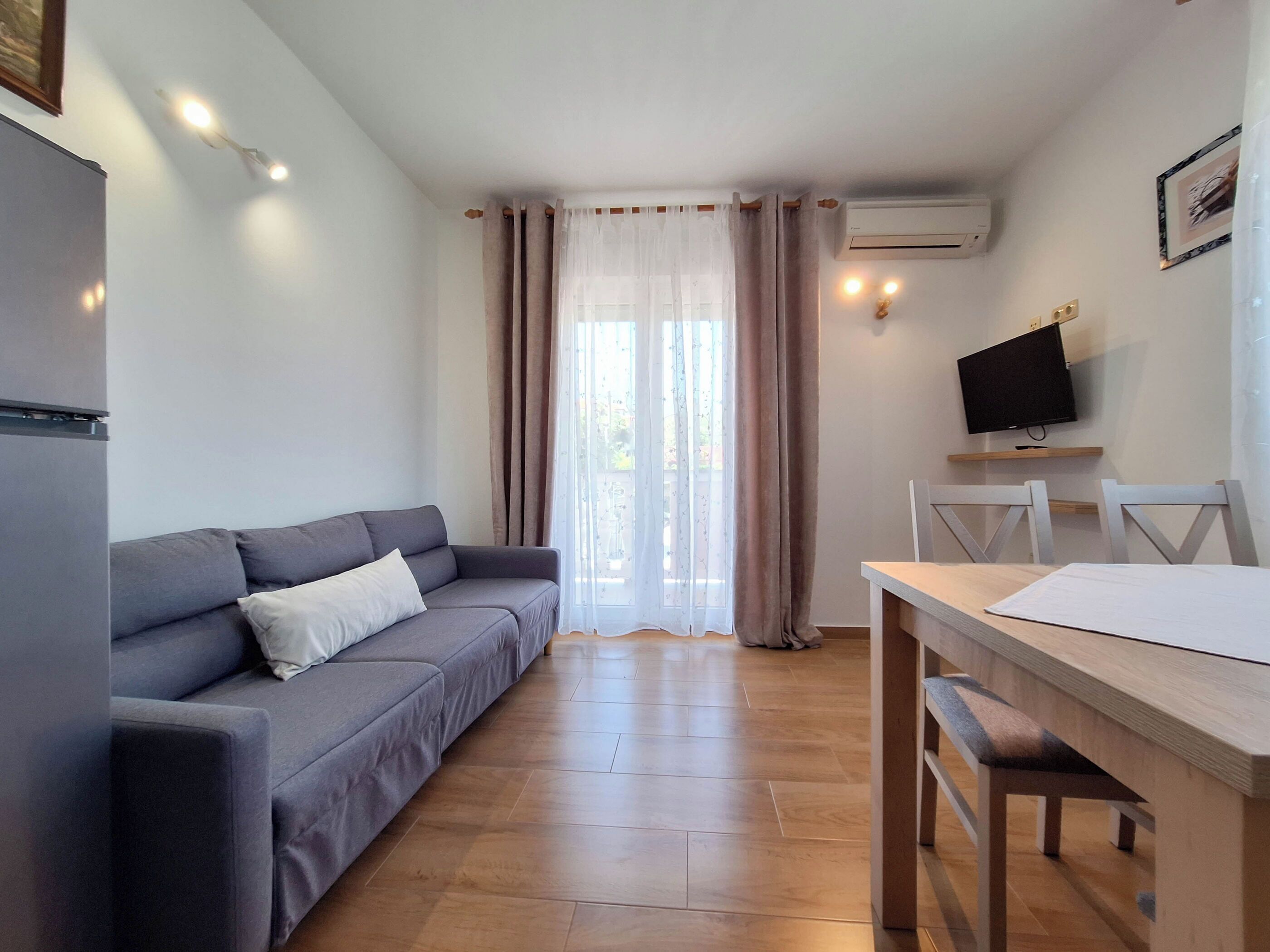 Una sala de estar moderna con un sofá gris, una mesa de comedor de madera y un televisor montado en la pared.