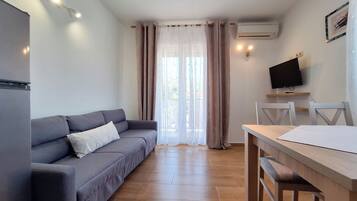 Una sala de estar moderna con un sofá gris, una mesa de comedor de madera y un televisor montado en la pared.