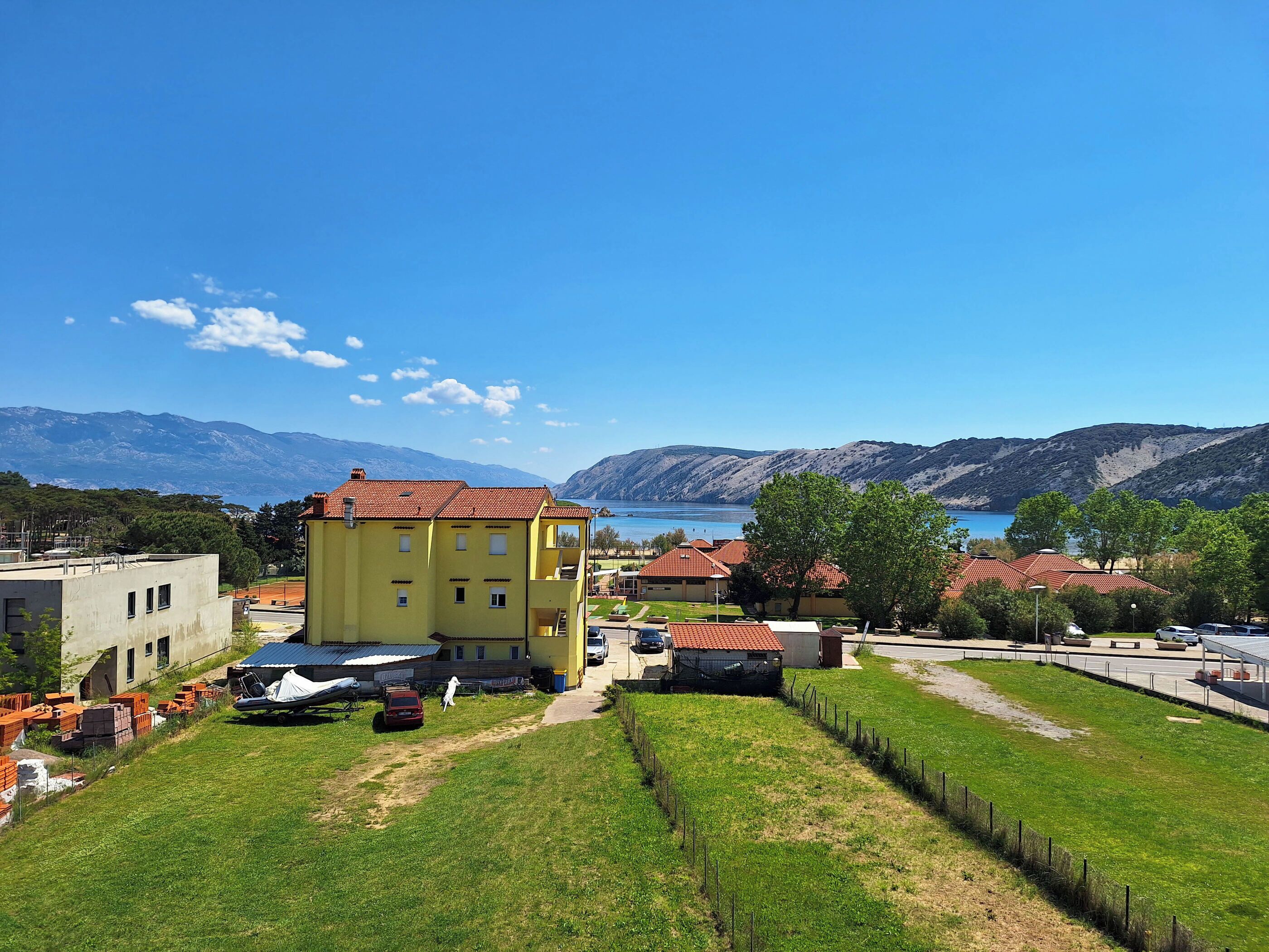 A yellow building with a red roof, surrounded by green grass and a clear blue sky.