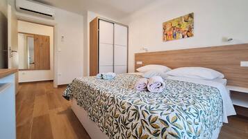 Habitación de hotel con cama, cabecera de madera, un cuadro en la pared y baño con espejo y puerta.