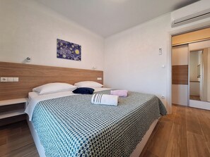 Une chambre à coucher avec une tête de lit en bois, un lit recouvert d’une literie à motifs, un tableau accroché au mur et une porte donnant sur une salle de bain.