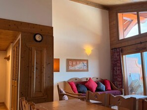 A cozy room with a wooden dining table, a sofa with colorful cushions, a clock on the wall, and a framed picture. - Cozy 3-room apartment near slopes with parking (Les Carroz d'Arâches)