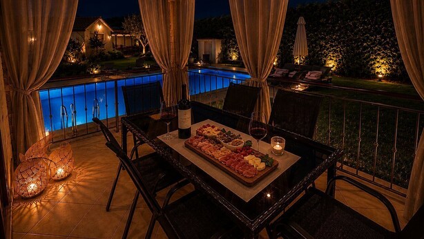 Een terras met uitzicht op een zwembad, een houten plafond en een gedekte tafel met eten en drinken.