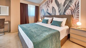 A hotel room with a large bed, a bedside table with a lamp, a chair, and a wall with a floral mural. - Villa Astrid (Rasa)