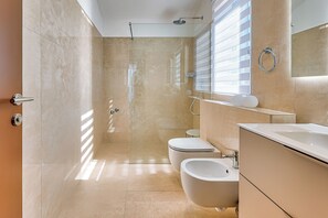 Un baño moderno con ducha de vidrio, inodoro, bidé y tocador con espejo.