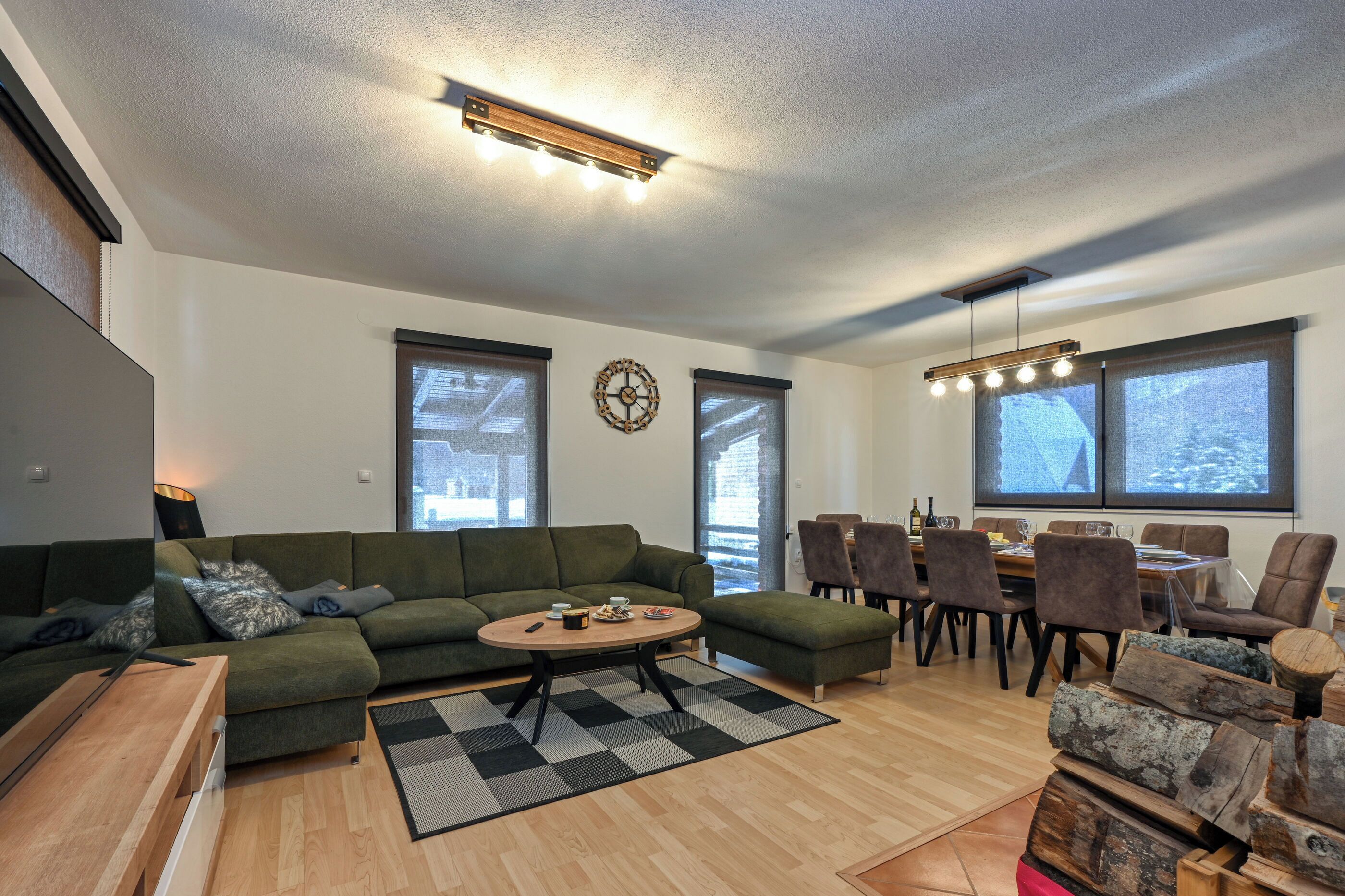Uma sala de estar moderna com um sofá verde, uma mesa de centro redonda e um espaço de jantar com cadeiras e mesa de madeira.