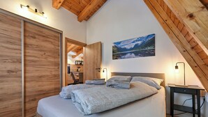 A bedroom with a large bed, wooden ceiling beams, a desk, and a painting of a mountain landscape. - Apartments AVA (Ogulin)