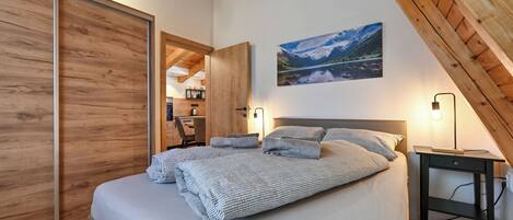 Un dormitorio con una cama grande, vigas de madera en el techo, un escritorio y un cuadro de un paisaje montañoso.