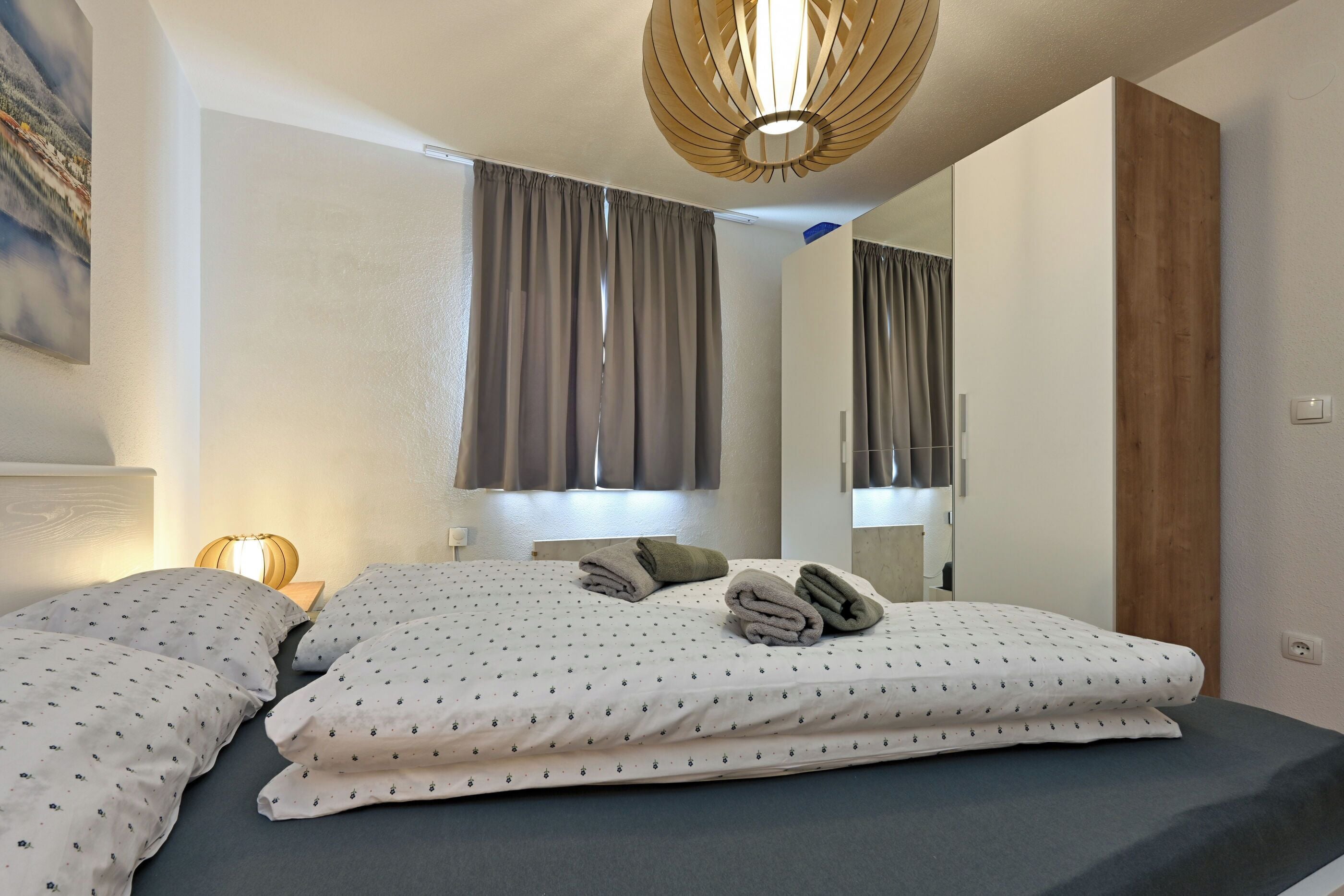 A neatly made bed with pillows and towels, a bedside lamp, and a large mirror.
