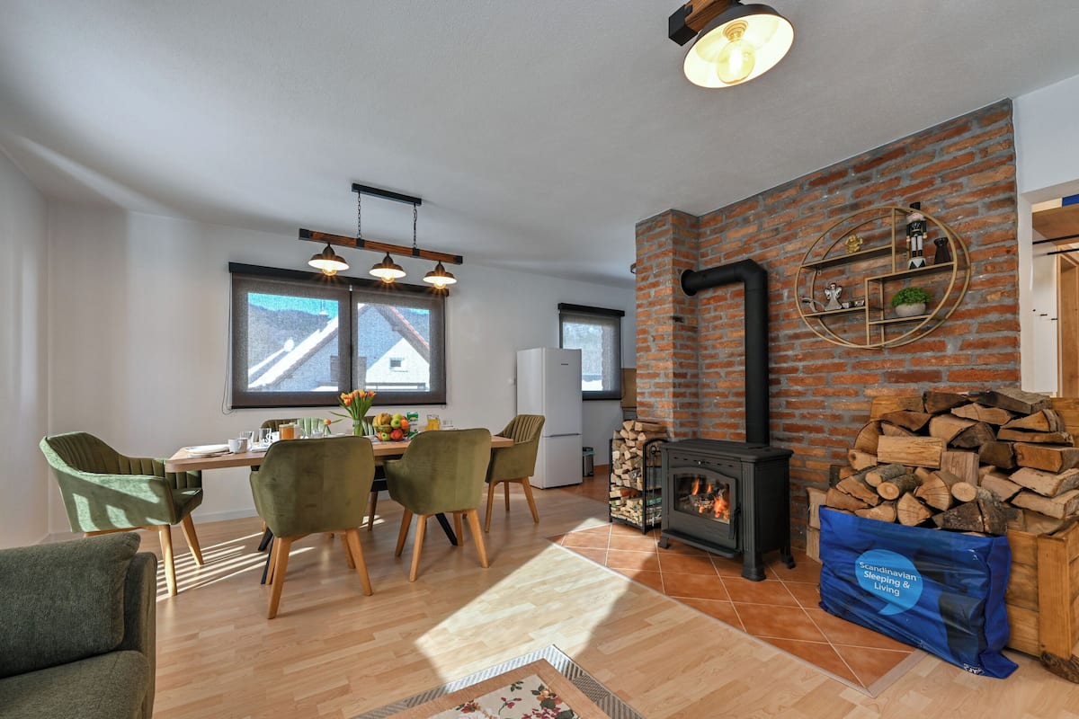 Ein modernes Wohnzimmer mit Backsteinwand, Kamin, Essbereich mit Stühlen und einem großen Fenster.