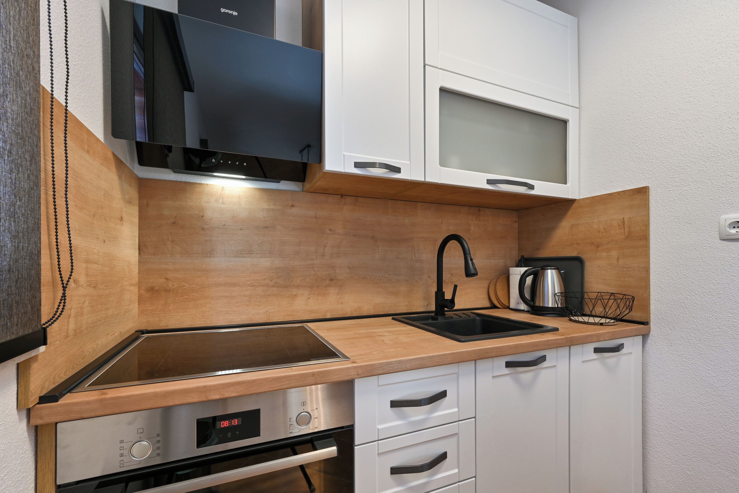 Cozinha moderna com bancada de madeira, eletrodomésticos de aço inoxidável e armários brancos.