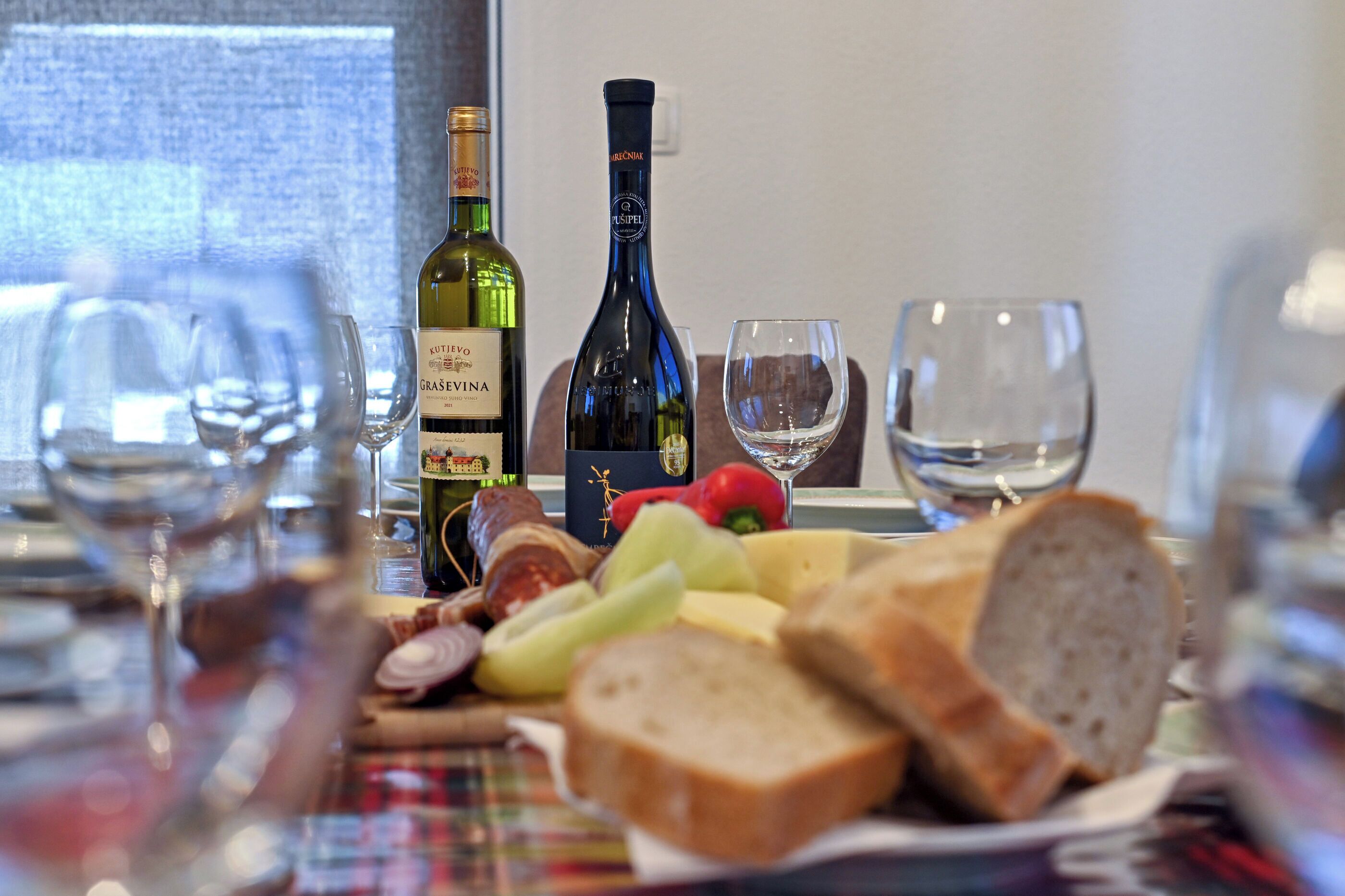 Ett bord med en flaska Gräsvina-vin, en flaska vin och olika livsmedel, inklusive bröd, ost och grönsaker.