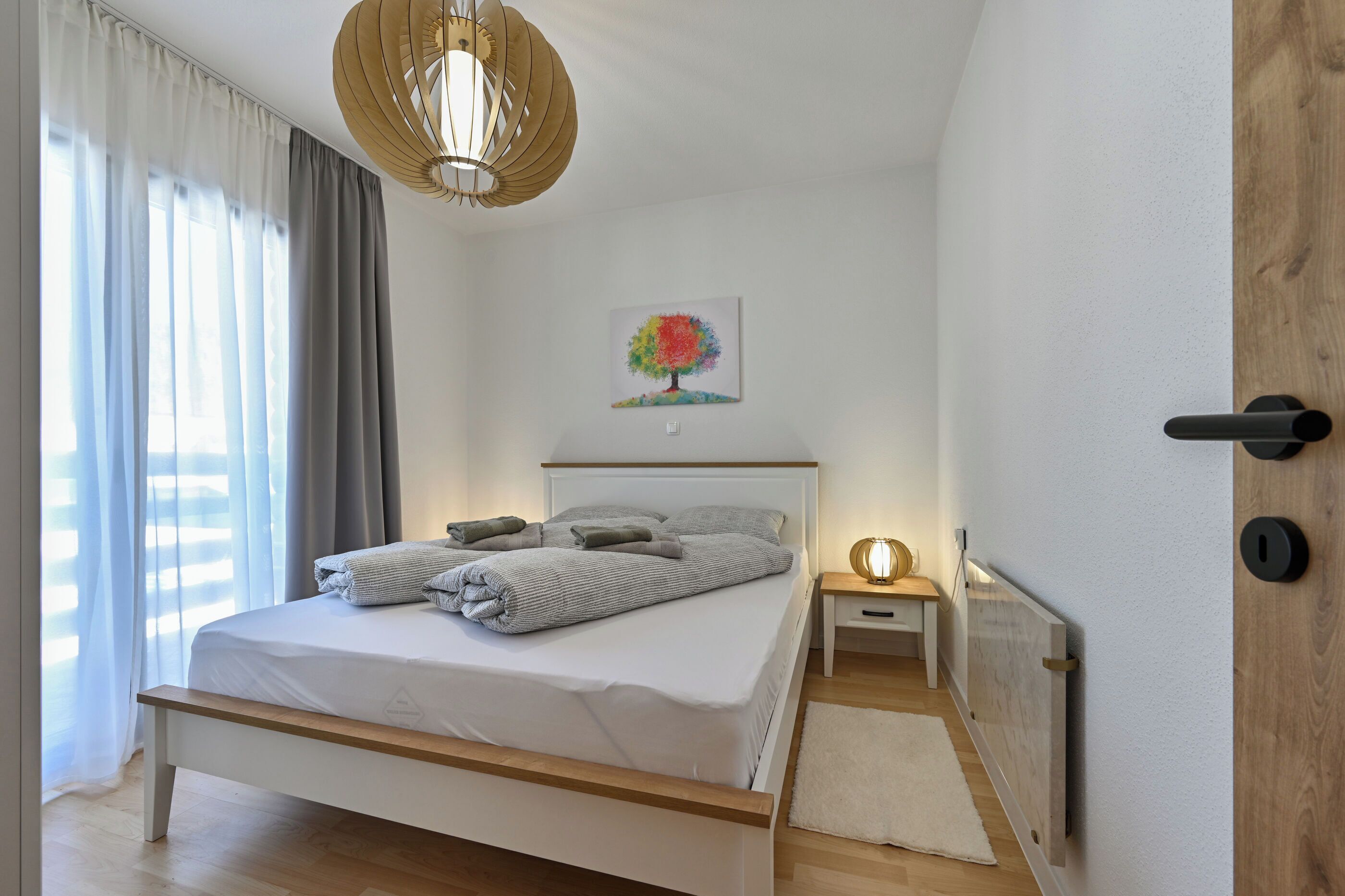 A bedroom with a bed, bedside table, lamp, and a painting on the wall.