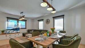 A modern living room with a dining area, large windows, and a flat-screen TV. - Apartments AVA (Ogulin)