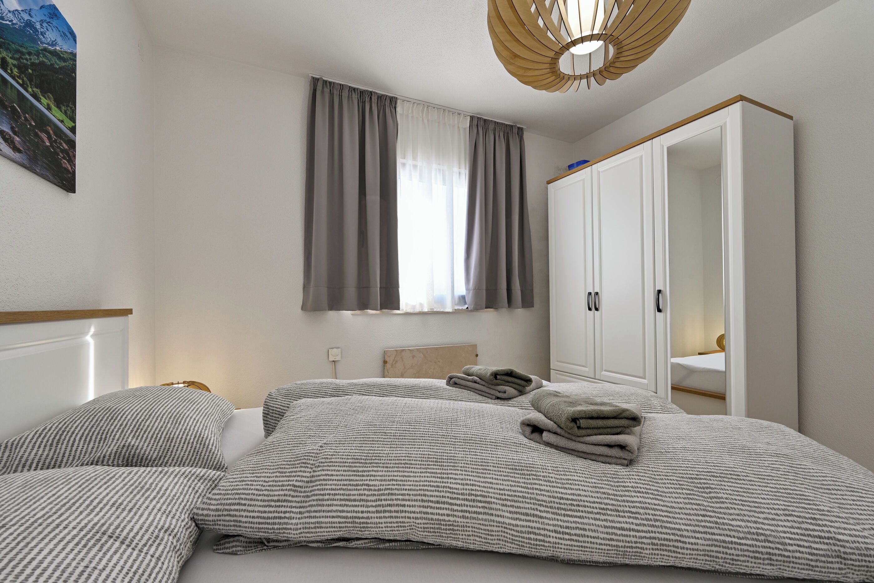 A bedroom with a bed, a wardrobe, a window with curtains, and a wall-mounted light fixture.