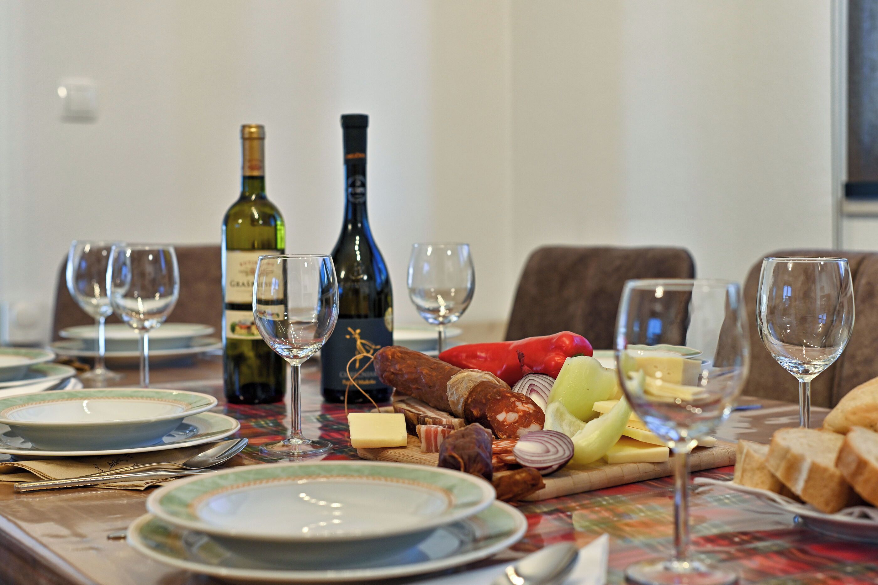 Une table à manger dressée avec des assiettes, des couverts, une bouteille de vin, des verres et une variété d’aliments, notamment du fromage, du pain et des légumes.