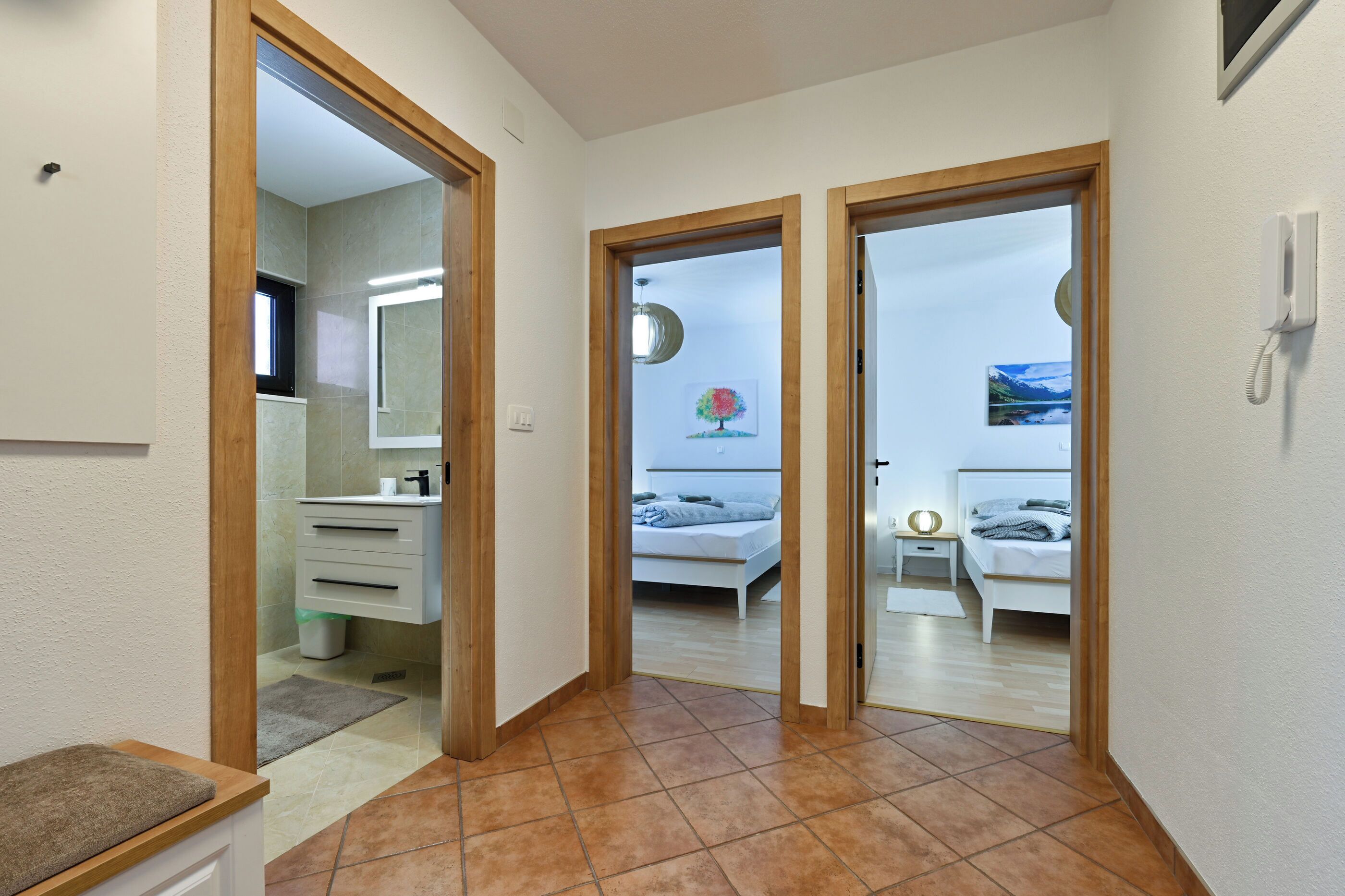 A hallway with a bathroom on the left, a bedroom with a bed and nightstand, and a second bedroom with a bed and nightstand.