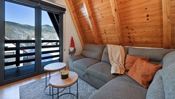 A cozy room with a grey sofa, a small round table, and a large window offering a view of a snowy landscape. - Apartments AVA (Ogulin)