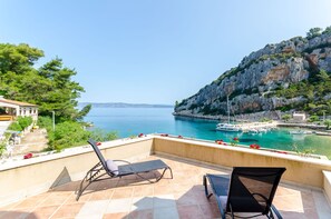 A balcony with two lounge chairs overlooking a coastal marina with boats and a rocky cliff. - Apartments Serzane (Jelsa)