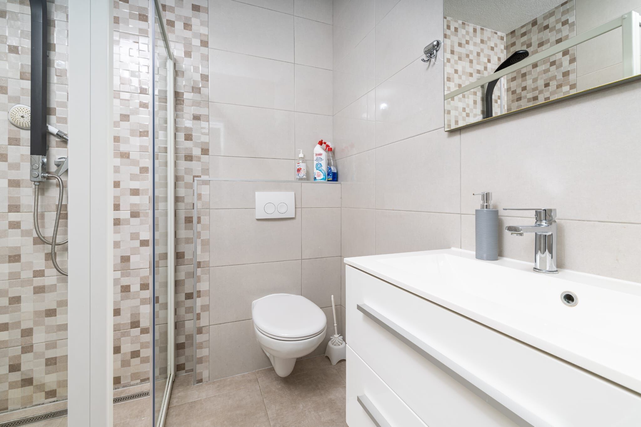 A modern bathroom with a glass-enclosed shower, a white toilet, and a white sink with a mirror above it.