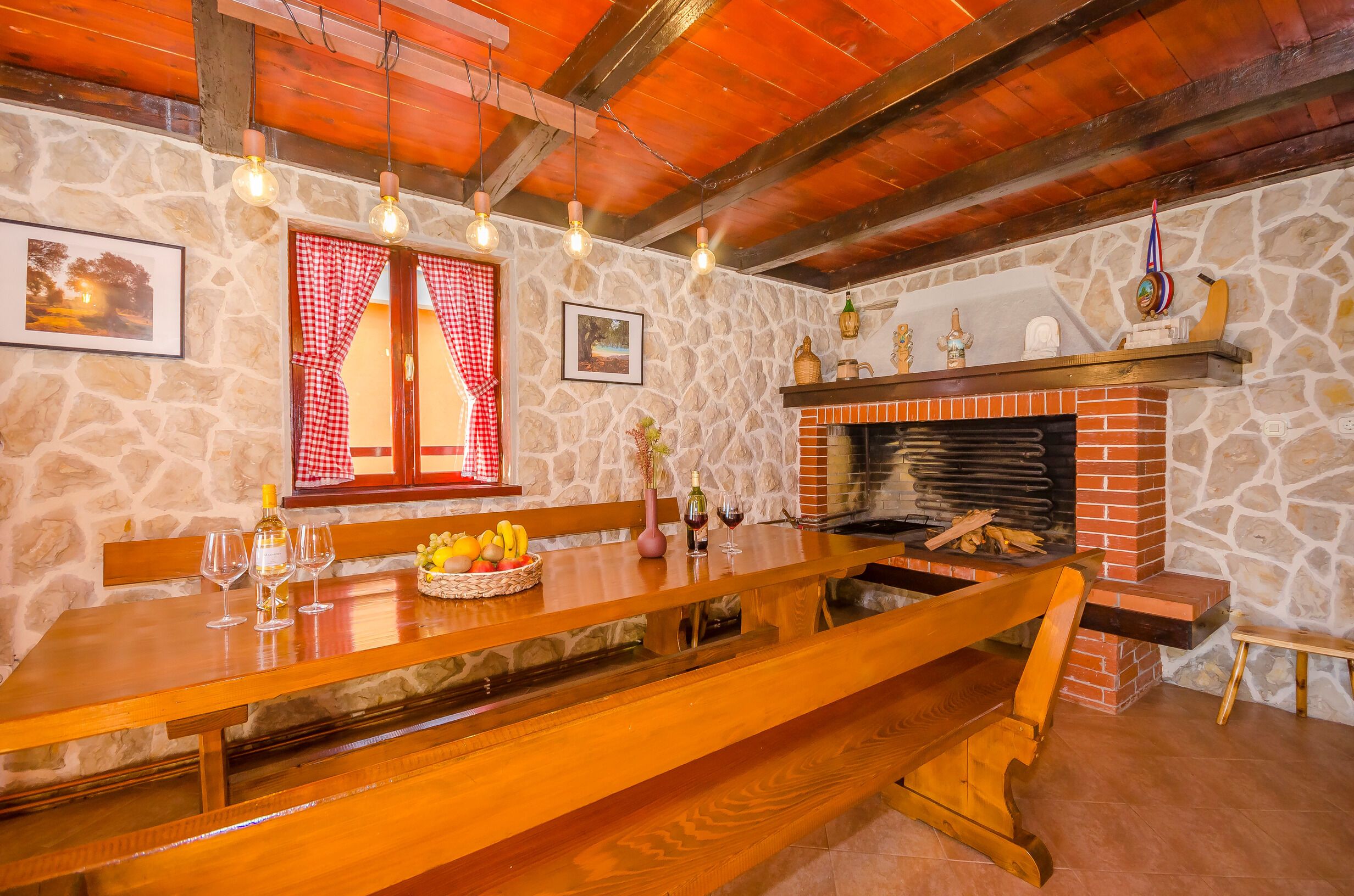 Un intérieur rustique avec un mur en pierre, des poutres en bois au plafond, une cheminée et une table en bois sur laquelle sont disposés des verres à vin et des fruits.
