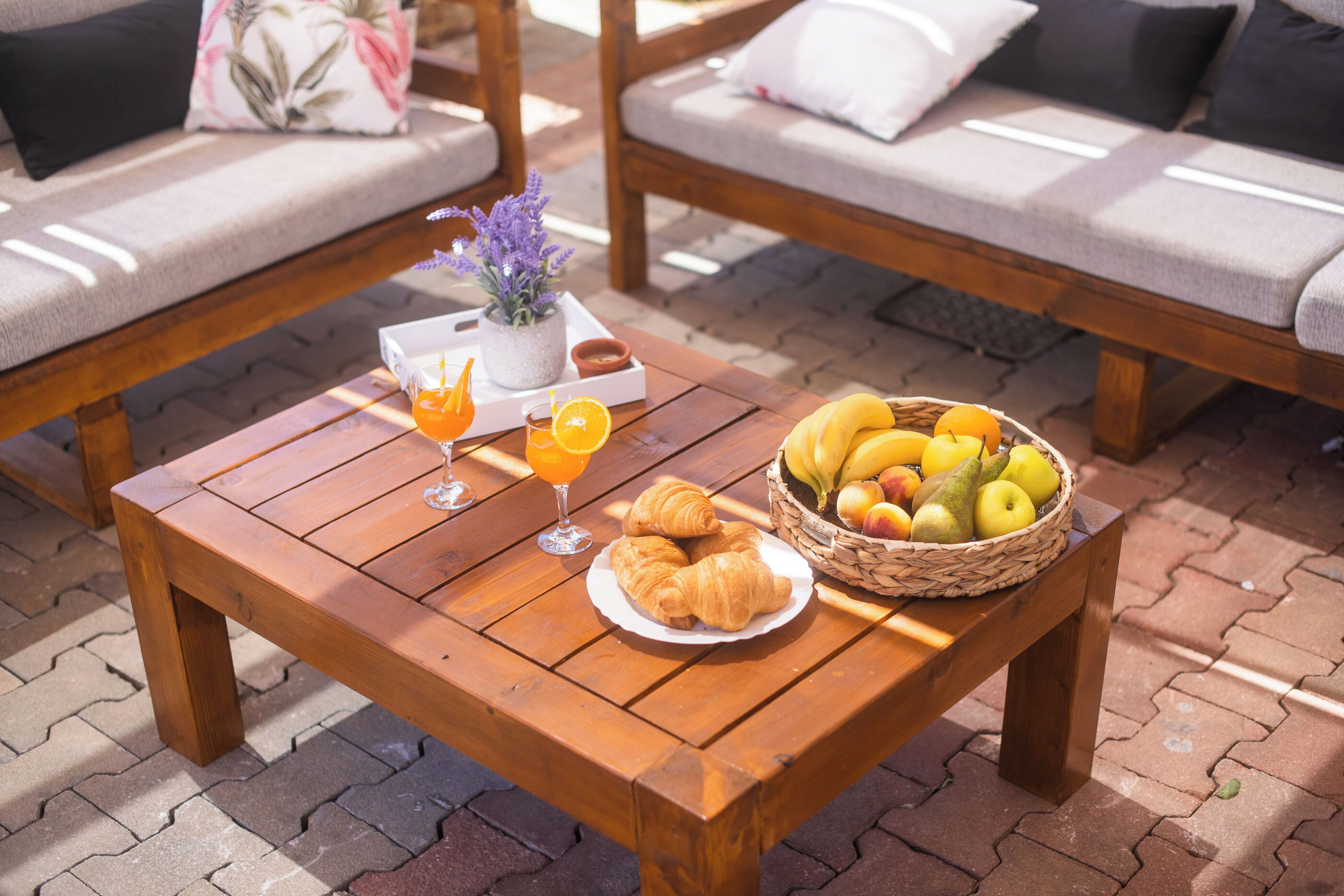 A wooden table with a basket of fruit, two glasses of orange juice, and a plate with croissants.