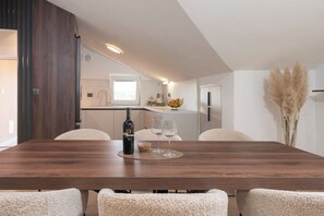 A modern dining area with a wooden table, four chairs, a bottle, and two wine glasses. - House Leonardo (Galovac)