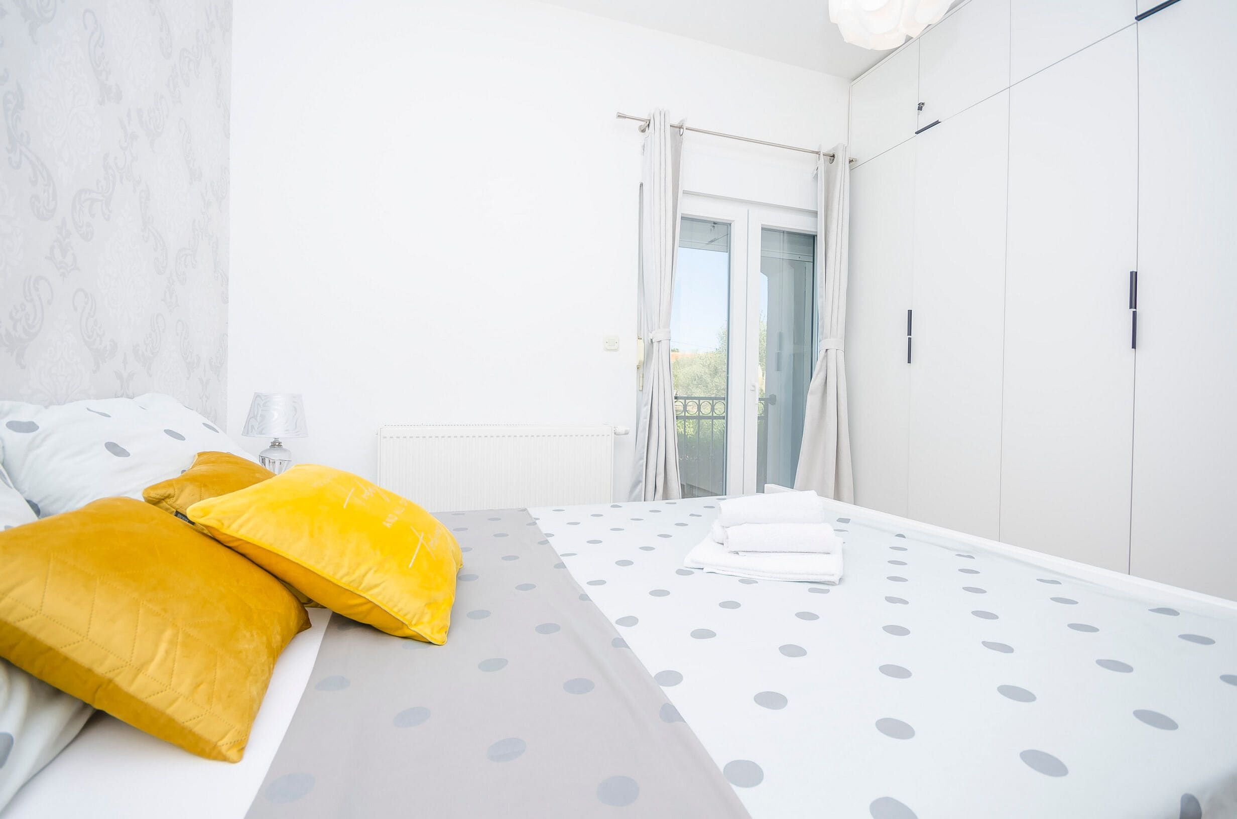 Een slaapkamer met een bed, kussens, een radiator, een raam met gordijnen en een garderobe.