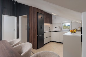 A modern kitchen with wooden cabinets, a black refrigerator, and a white countertop. - House Leonardo (Galovac)