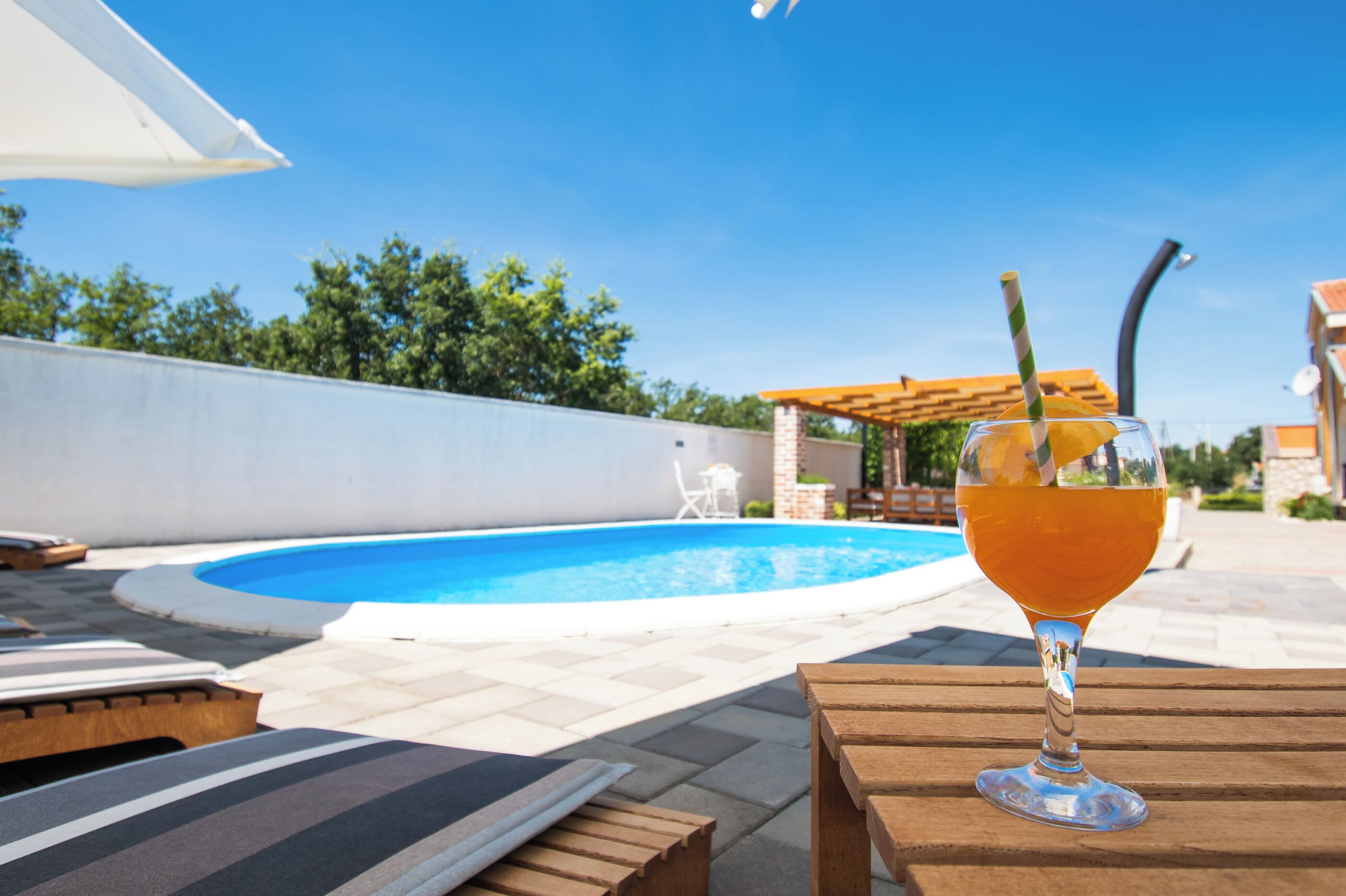 Un verre d’une boisson ambrée posé sur une table en bois, avec une piscine en arrière-plan.