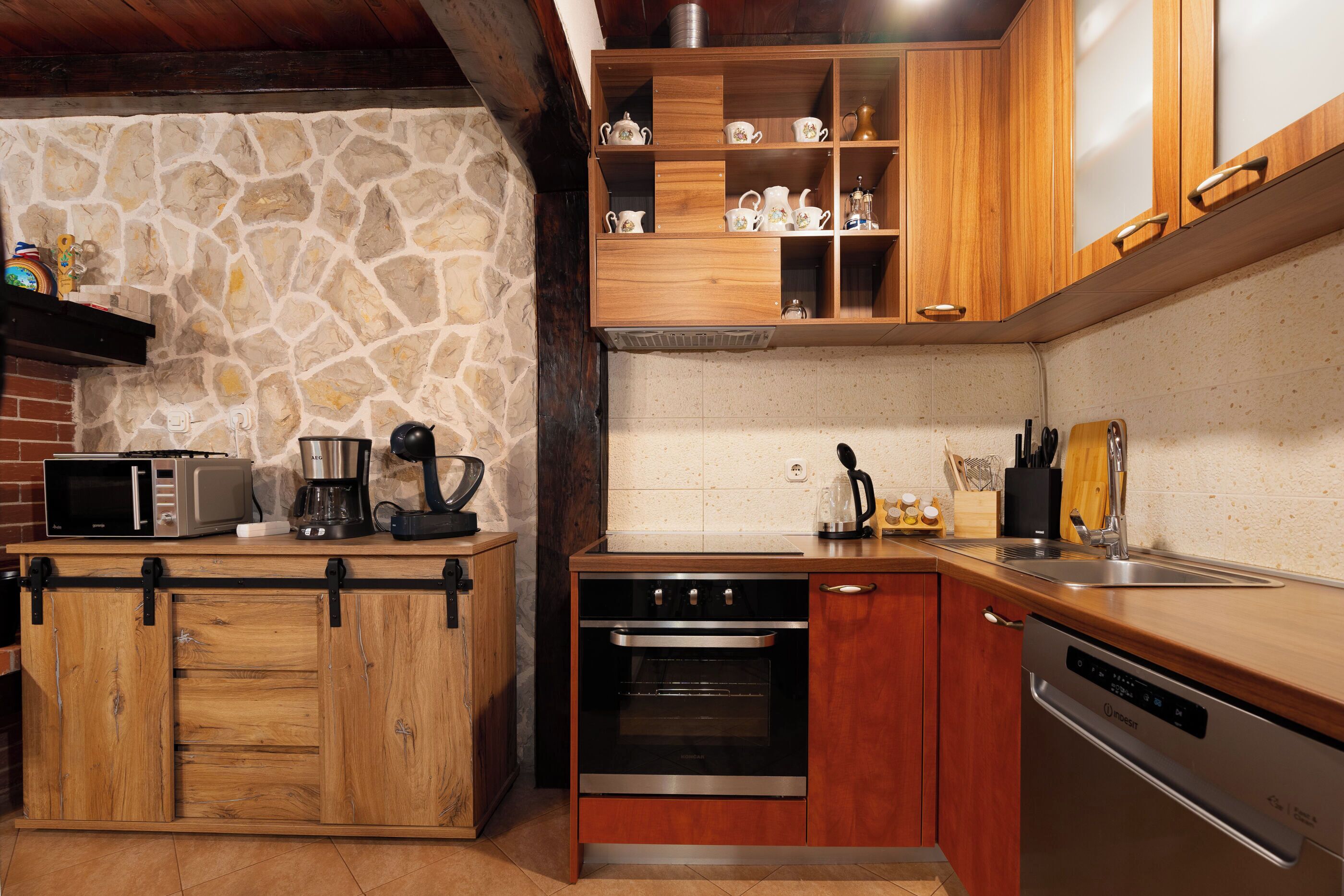 A kitchen with wooden cabinets, a stone wall, a microwave, a coffee maker, and a dishwasher.