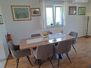 A dining area with a wooden table, six grey chairs, a bowl of fruit, and a window with curtains. - Villa Zelena Oaza (Labin)