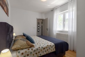 A bedroom with a bed, a nightstand, a lamp, and a window with curtains. - Villa Zelena Oaza (Labin)