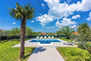 A swimming pool with lounge chairs, a palm tree, and a clear blue sky. - Villa Zelena Oaza (Labin)